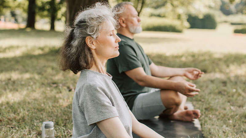 Older man and woman sitting with hands on knees meditating in a park